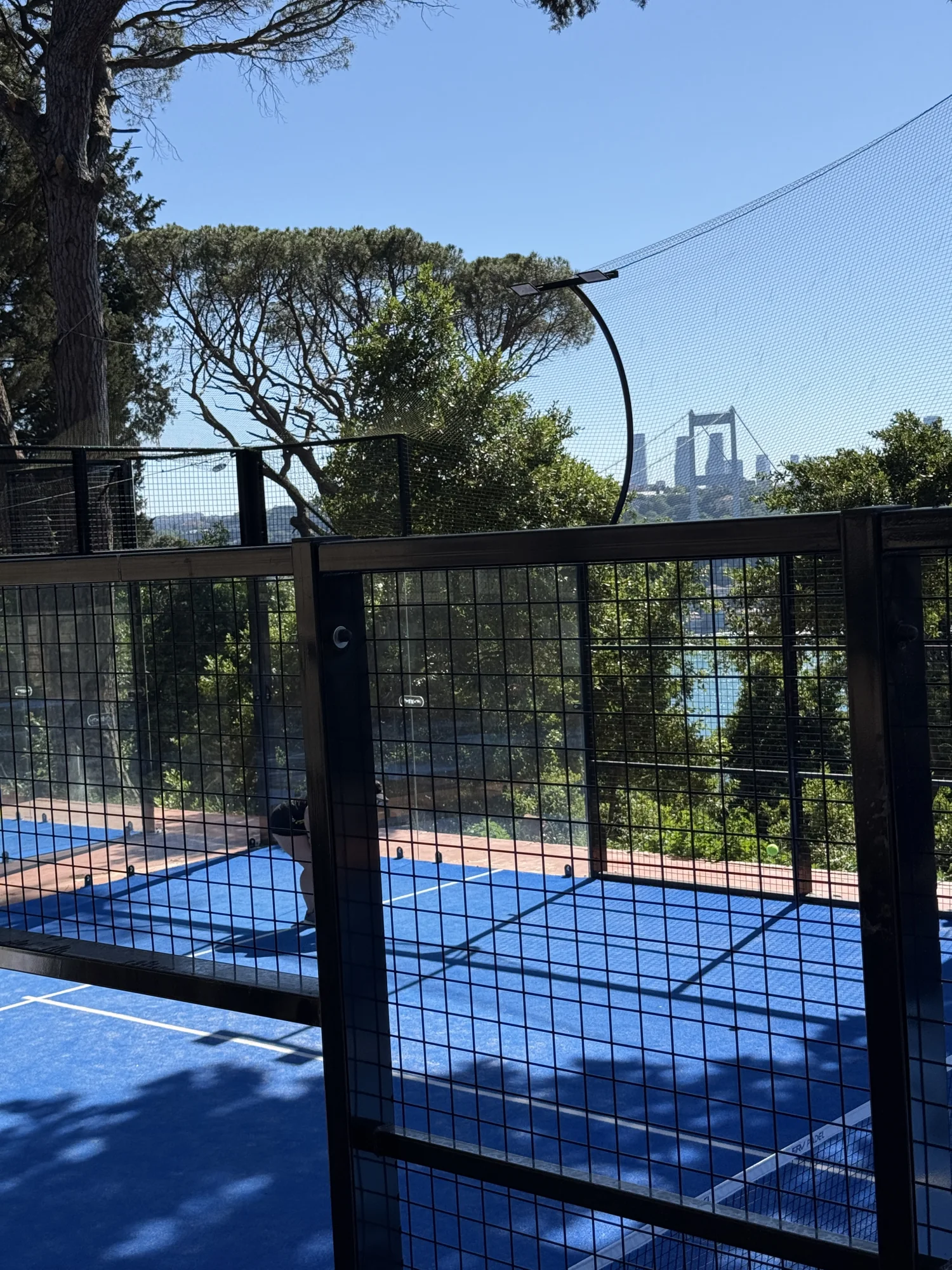 A blue More Padel court among trees with the Bosphorus Bridge in the distance